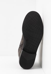 Chaussure en daim gris avec une semelle en caoutchouc noire  à motif. La chaussure présente un design élégant et une fermeture éclair latérale pour un accès facile. Taille indiquée : 37.