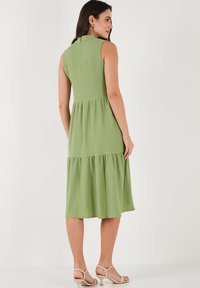 Green, tiered, sleeveless dress in textured fabric with a back closure; knee-length with a flowing silhouette. Minimalistic design details.
