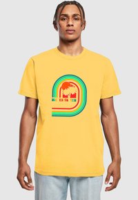 Geltona medvilnės marškinėliai su daugiakryptėm grafikomis, kuriose vaizduojami palmių medžiai ir saulė, papuošti tekstu "ROLLER SKATER CLUB VENICE BEACH."