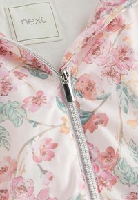 Veste légère à fermeture éclair zippée présentant un motif floral dans des tons rose et vert, avec une fermeture éclair argentée et une étiquette portant la mention "next".