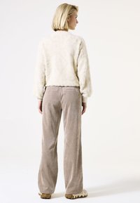 Suéter cremoso y esponjoso de manga larga, combinado con pantalones de pana beige. Los pantalones son de pierna ancha con una textura suave.