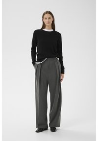 Must kampsun valge kraega särgi kohal, kombineeritud kõrge vöökohaga laiade hallide pükstega. Valitsevad sujuvad tekstuurid ja neutraalsed värvid.