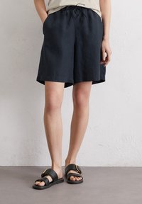 Donkerblauwe linnen shorts met een elastische tailleband en trekkoord, zijzakken en een iets losser model. Gepaard met zwarte sandalen.