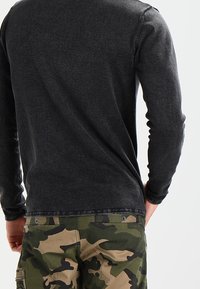 Camiseta negra de manga larga con textura suave y cuello redondo, combinada con pantalones cargo de camuflaje verde con bolsillos y costuras reforzadas.
