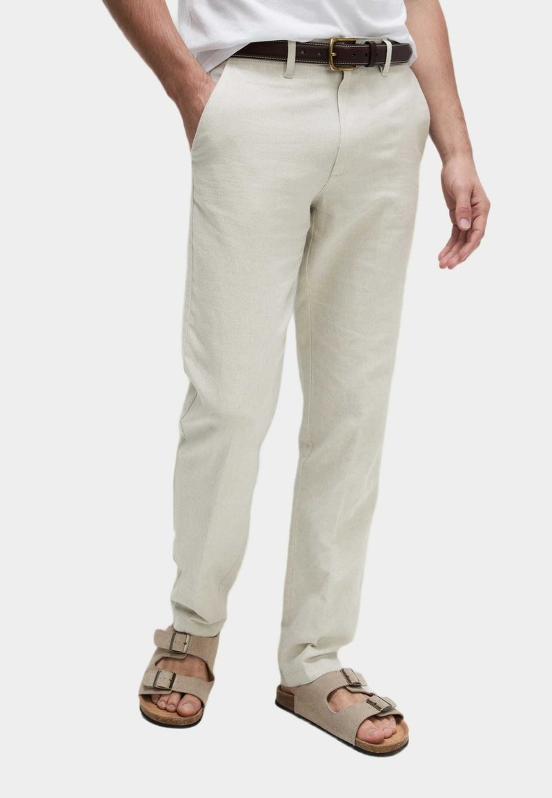Pantalones de lino color beige claro con un corte relajado, que cuentan con bolsillos laterales. Combinados con un cinturón de cuero marrón y sandalias cómodas con hebillas.