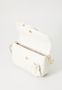 Sac à bandoulière en cuir blanc avec une fermeture à bouton pression dorée, doublure intérieure et un accent floral sur le devant. Texture lisse et forme structurée.