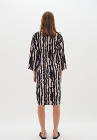 Robe mi-longue en tissu beige avec des rayures verticales noires, dotée de manches larges et d'une taille cintrée. Texture lisse, minimalisme dans les détails.