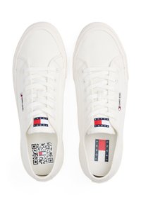 Baskets en toile blanche avec une semelle en caoutchouc, dotées de lacets centraux, d'étiquettes logo et d'un code QR sur la semelle intérieure. Design épuré et profil plat.