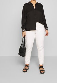 Camicia nera con bottoni e colletto a fantasia, pantaloni bianchi a gamba dritta, borsa a tracolla nera intrecciata e sandali neri. Tessuto morbido e vestibilità rilassata.