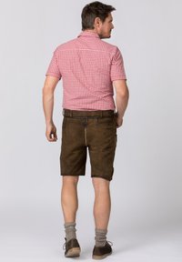 Röd och vit rutigt kortärmad skjorta, ihopparad med bruna lädershorts. Grå strumpor och mörka skor kompletterar outfiten, sedd bakifrån.