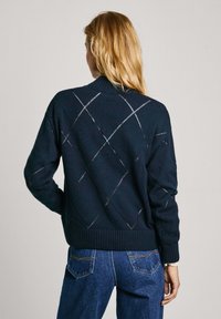 Navy gebreide trui met een ruitenpatroon, voorzien van een hoge kraag en geribbelde manchet. De achterkant toont opensteekdetails.