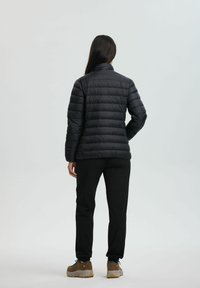 Sort puffjakke med horisontalt quiltet design, høj krave, lange ærmer, parret med sorte bukser og brune vandresko.