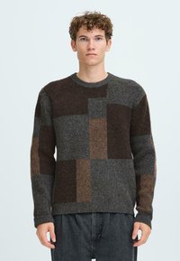 Strickpullover mit einem Patchwork-Design in Grautönen, Braun und Rost. Er hat einen runden Ausschnitt und gerippte Bündchen, mit einer strukturierten Oberfläche.