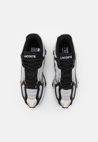 Sneakers Lacoste w czerni i szarości, z siateczkową cholewką, warstwową konstrukcją i teksturowanymi detalami. Czarny sznurówki i logo na języku.