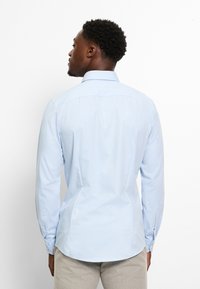 Camicia azzurro chiaro a maniche lunghe con colletto strutturato, polsini con bottoni, orlo curvo e texture liscia.
