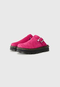 Pink suede clogs with a closed toe, adjustable silver buckle, and black rubber sole featuring yellow stitching and a textured tread pattern.