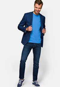 Granatowa marynarka w kratę nałożona na niebieską koszulkę, w zestawie z ciemnymi dżinsami i niebieskimi sneakersami. Posiada nowoczesny krój i teksturowany materiał.