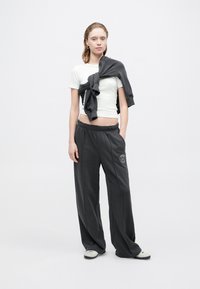 Luźne szare dresy z elastycznym paskiem w talii i boczną kieszenią, w zestawieniu z dopasowaną białą koszulką oraz szarym swetrem swobodnie zarzuconym na ramiona.