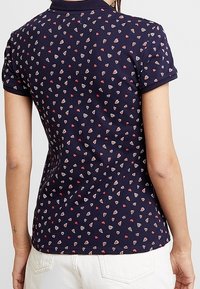 Marinblå polotröja med ett spritt hjärtmönster i röd och vit. Korta ärmar, krage och en figurnära siluett.