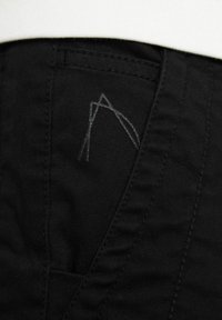 Tela negra con un acabado texturizado, que presenta un diseño de costura gris en contraste en un bolsillo. Líneas limpias y corte ajustado.