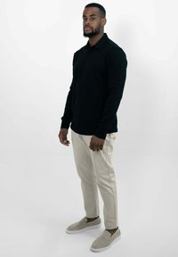 Schwarzes langärmliges Polo-Shirt, beige Hosen und beige Slipper. Das Shirt hat einen klassischen Kragen und Knöpfe, im Slim-Fit-Design.