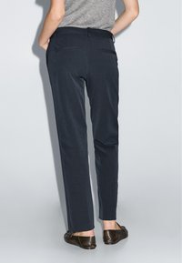 Op maat gemaakte marineblauwe broek met een zachte textuur, twee achterzakken en een rechte pasvorm, gecombineerd met bruine platte schoenen.