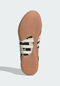 Black and white patterned athletic shoe with three white stripes, a rubber sole, and a textured brown outsole featuring a logo.