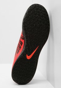 Zapatilla deportiva roja y negra con una suela texturizada que presenta un patrón hexagonal y un acento destacado del logo de Nike en rojo.