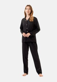 Conjunto de pijama negro con lunares que incluye una camisa de botones con cuello en pico y pantalones a juego. Fabricado en un tejido suave con un corte relajado.