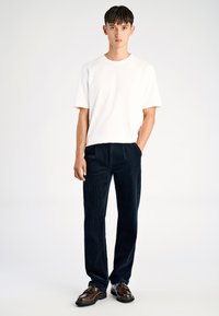 Wit katoenen T-shirt met korte mouwen, gecombineerd met marineblauwe corduroy broek met verticale strepen en bruine leren schoenen.