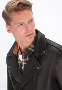 Jachetă de biker din piele neagră, cu rever largi și nasturi tip snap, purtată peste o cămașă în carouri cu nuanțe de albastru, portocaliu și alb.
