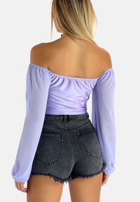 Lilla off-shoulder top med lange, gennemsigtige ærmer; tætsiddende liv. Sammen med højtsiddende, fransede sorte denimshorts.