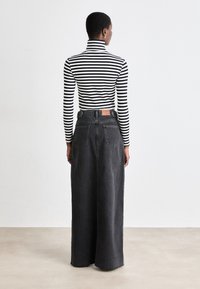 Črna denim krila širokega kroja, v kombinaciji z oprijetim črno-belih prugastim rolkom. Ima dve hrbtni žep in usnjeno oznako.
