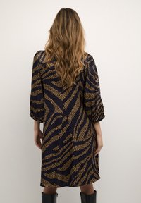 Marindräkt i marinblått med ett leopardmönster i guld, med trekvartslånga ärmar och en avslappnad passform, tillverkad av ett lätt tyg.