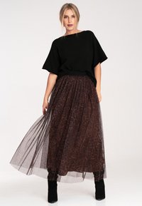 Czarna, oversize'owa bluzka w połączeniu z brązową, tiulową spódnicą maxi w panterkę. Spódnica ma marszczoną talię i fakturowane warstwy.