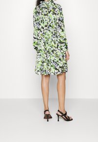 Floral dress with long sleeves; black background with green and white flowers; loose fit; paired with strappy black high-heeled sandals.