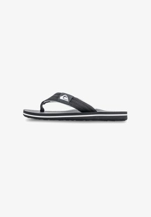 Svart flip-flop med ett tygrem, strukturerad sula och en kontrasterande vit logodetalj. Har en platt design och gummisula.