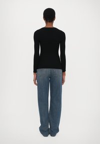 Svart ribbet langermet topp med en tettsittende silhuett, parret med blå vide jeans med detaljer på baklommene og en avslappet passform.