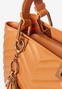 Tanfarbene, gesteppte Handtasche mit einem strukturierten Muster, goldfarbener Hardware und einem dekorativen Quast-Akzent an einem Schlüsselanhänger. Glattes Material und strukturierte Gestaltung.