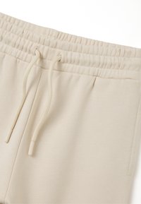 Beige joggings met een elastische tailleband, verstelbaar trekkoord en een gladde, zachte textuur. Heeft zijzakken en een casual ontwerp.