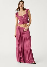 Zweiteiliges Outfit in tiefem Pink. Das Oberteil hat geraffte Träger und ein Bindedetail; der Rock verfügt über gestufte Lagen und einen elastischen Bund.