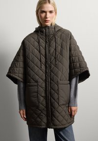Poncho trapuntato di colore verde oliva scuro con cappuccio, due tasche frontali e maniche corte. Presenta un cordoncino e una texture a rombi.