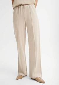 Beżowe, miękkie spodnie z luźnym krojem, posiadające elastyczny pasek, zakładki i proste nogawki. W zestawie z butami na spiczastym nosku.