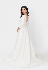 Weißes Kleid mit langen Ärmeln und V-Ausschnitt, fließendem Rock, glatter Textur und Knopfverschluss an der Rückseite. Klassisches und minimalistisches Design.