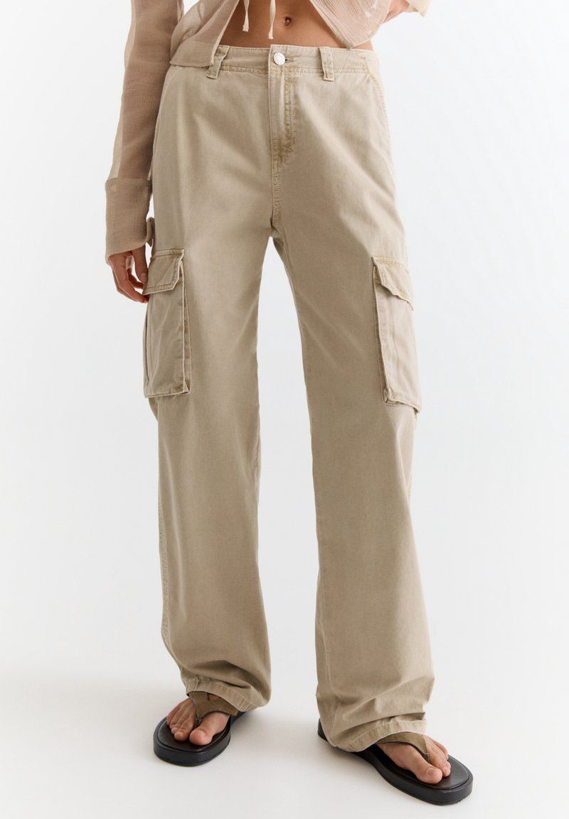 Pantalons cargo beiges avec une coupe droite, fabriqués en tissu léger. Comprend deux poches latérales et une fermeture à bouton à la taille.