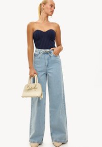 Marineblauw pinstripe bodypak, lichtblauwe high-waisted jeans met wijde pijpen, beige gestructureerde handtas en nude hakken.