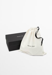 Svart rektangulär låda och vit dragsko-påse med svart snöre, båda märkta med "Massimo Dutti"-logotyp på en vit bakgrund.