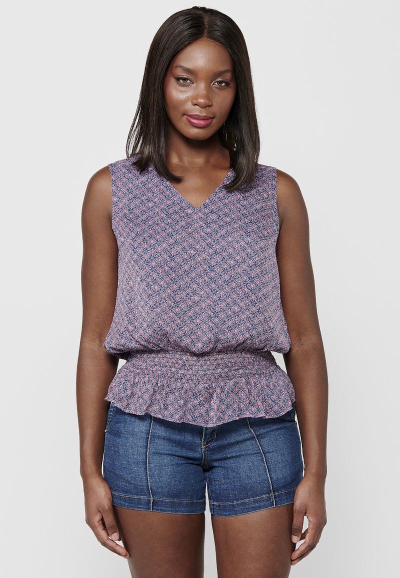 Mouwloze blouse in een roze en blauwe bloemenprint, met een v-hals ontwerp en een geraffineerde tailleband; gecombineerd met denim shorts met een omgeslagen zoom.