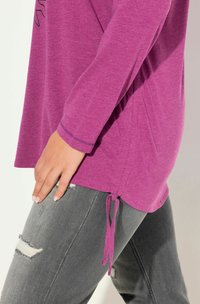 Violetti pitkähihainen paita, jossa on sivusiteet, yhdistettynä harmaisiin kuluneisiin farkkuihin, joissa on revittyjä paikkoja. Sujuva pinta, rento istuvuus.