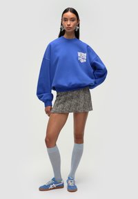 Sudadera azul de gran tamaño con gráfico blanco, combinada con una falda corta de pata de gallo, calcetas altas de color azul claro y zapatillas azules.